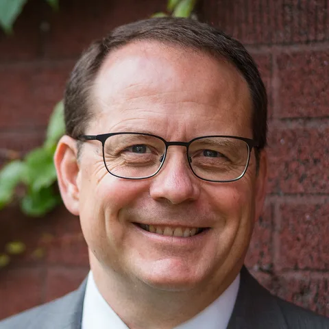 Mike Schreiner, smiling, in front of a brick wall in 2021